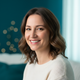 A happy woman in her late 30s smiles warmly, conveying trust and satisfaction. The background is a soft blur of deep teal and